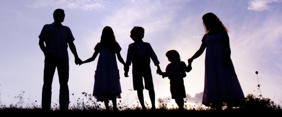 Family of five standing together in a field holding hands as the sun sets