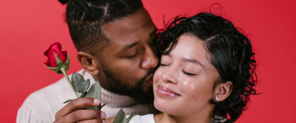Interracial couple kissing each other and celebrating Valentine's day with roses